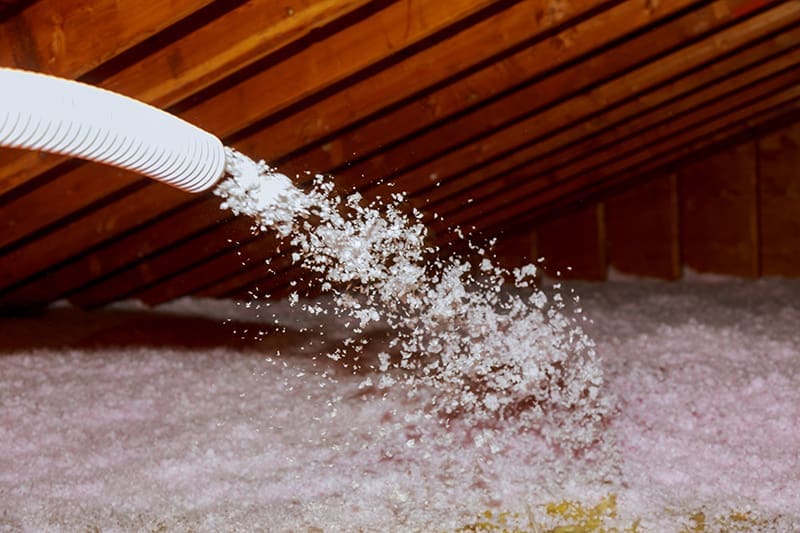 Spraying Blown Fiberglass Insulation for roof - technician spraying foam insulation using plural component gun pest insulation services